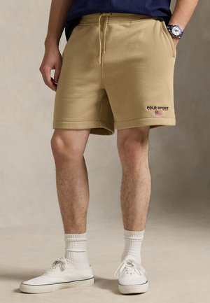 Μπεζ βαμβακερά σορτς με ελαστική μέση και κορδόνι, με πλαϊνές τσέπες και μικρό λογότυπο "Polo Sport". Φορεμένα με λευκά αθλητικά παπούτσια.