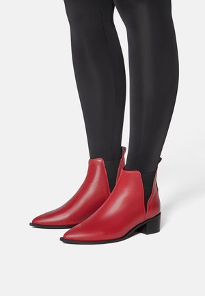 Stivaletti ankle in pelle rossa con punta affusolata, pannelli laterali elastici neri e tacco basso a blocco. Texture liscia con dettagli di accentuazione minimi.