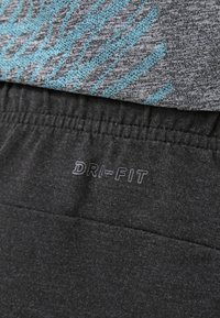 Tela atlética gris con un patrón abstracto en tono teal en la parte superior, cintura de jogger negra DRI-FIT en la parte inferior, que presenta una textura suave y banda elástica.