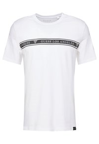 Bílý bavlněný tričko s černým vodorovným pruhem a nápisem "GUESS LOS ANGELES", krátké rukávy a kulatý výstřih.