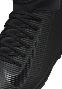 Zapatilla deportiva negra con una superficie texturizada, cordones prominentes y un logo negro brillante. El diseño incluye patrones de rayas sutiles.