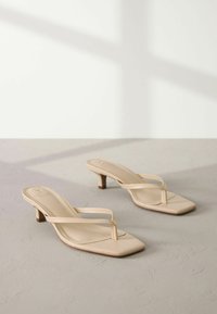 Sandales en cuir beige à lanières avec orteils carrés, fines lanières et talons blocs de 5 cm, reposant sur une surface gris texturée.