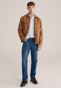 Rjava jakna iz semiša čez svetlo modro zgornji del z zadrgo, kombinirana z modrimi kavbojkami in črnimi čevlji z resicami. Neformalna, večplastna obleka.