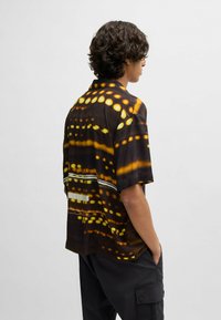 Short-sleeve shirt in black fabric with a yellow and white geometric pattern. Features a camp collar and relaxed fit.