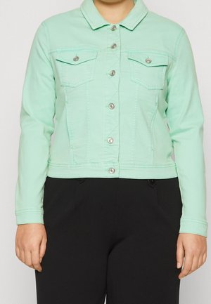 Personne portant une veste boutonnée vert clair avec poches poitrine et manches longues, associée à un pantalon noir.