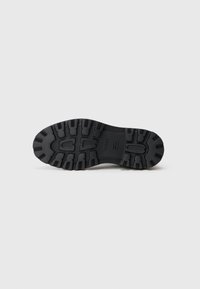 Sole in gomma nera e robusta con profonde scanalature, logo "BOSS" in rilievo e aree di presa testurizzate su uno sfondo bianco uniforme.