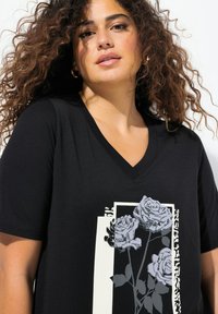 Camiseta negra de cuello en V hecha de tela suave, con un diseño gráfico de rosas grises sobre un fondo blanco con acentos abstractos.