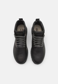 Botas de tobillo de cuero negro con cordones grises, costuras reforzadas y un lazo en la parte posterior. Textura suave con un diseño de punta redonda.
