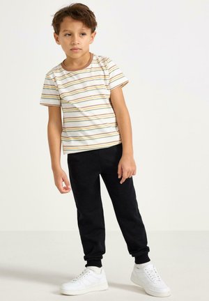 Randig t-shirt med korta ärmar i vitt med orange och gröna ränder, kombinerad med svarta mjukisbyxor och vita sneakers. Avslappnad passform, mjuk textur.