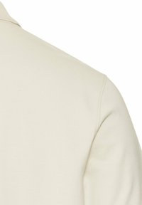 Lys beige pullover med et tekstureret stof. Har en blød krave og synlige sømme langs skuldrene og ærmerne.