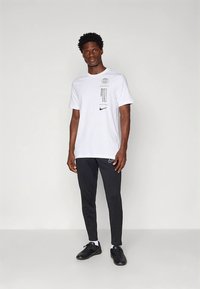 Camiseta blanca de manga corta con gráficos impresos y logo negro de Nike, combinada con pantalones negros de corte ajustado y zapatillas deportivas negras.