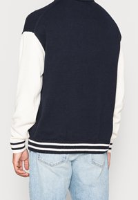 Suéter de punto azul marino y blanco con un cuello y puños acanalados, que presenta rayas horizontales en el dobladillo, diseñado con una manga en contraste.
