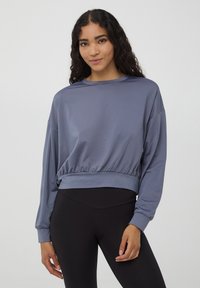 Fioletowy, krótki sweatshirt z długimi rękawami, okrągłym dekoltem i marszczonym dołem. Gładka tkanina o subtelnym połysku, zestawiona z czarnymi legginsami.