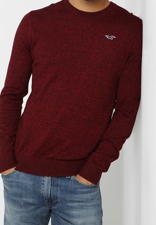 Punainen tekstuuri neule, jossa on pyöreä kaula-aukko ja ribbireunat, jossa on pieni valkoinen logo rinnassa. Yhdistetty sinisiin farkkuihin.