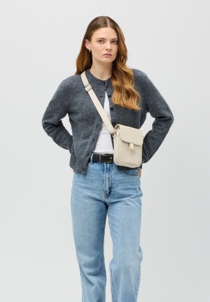 Cardigan grigio in lana con bottoni, indossato su una camicia bianca. Jeans azzurri a vita alta, abbinati a una borsa a tracolla beige.