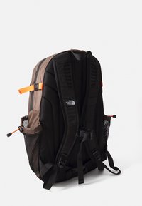 Barna és fekete North Face hátizsák párnázott pántokkal, oldalsó hálós zsebekkel és állítható narancs csatokkal, hátulról bemutatva.