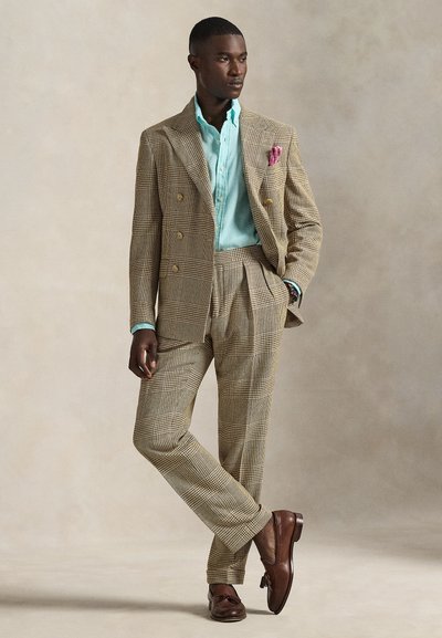 Traje cruzado de pata de gallo en beige y marrón, con camisa azul claro y pañuelo rosa en el bolsillo. Zapatos de cuero marrón completan el conjunto.