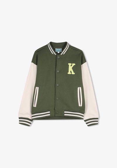 Veste universitaire verte avec manches crème, poignets et ourlet côtelés, arborant un écusson jaune en forme de "K" sur la poitrine et une fermeture à boutons pression.