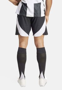 Pantaloni sportivi bianco e nero con un design geometrico, abbinati a calze alte nere con un'accenno bianca. Scarpe bianche visibili.
