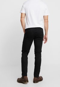 Zwarte slim-fit broek van een katoenmix, met een gladde textuur, vijf-pocket ontwerp en duurzame stiksels. G gedragen met bruine enkellaarsjes.