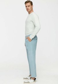 Hellgraues Langarmshirt kombiniert mit hellblauen Cordhosen. Sneaker mit weißen, grauen und schwarzen Akzenten. Seitenansicht des Outfits.