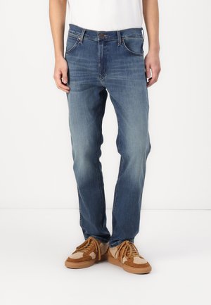 Denimjeans i middels blå, med fem lommer, knappestolpe og subtil fading. Kombinert med brune semskede og strikkesneakers.