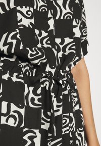 Tissu de robe à motifs noirs et blancs avec des dessins abstraits ; présente une taille cintrée avec un détail de cordon. Texture lisse.