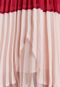 Vestido plisado con un diseño en capas, con la parte superior en rojo y una sección inferior fluida en rosa, confeccionado en una suave y transparente tela.