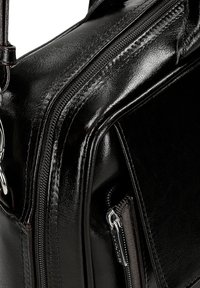 Černá kožená taška s lesklým povrchem, s kvalitním stříbrným zipem, elegantními liniemi a odolnou rukojetí. Obsahuje viditelné detaily prošívání.