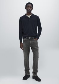 Dark navy long-sleeve polo shirt with a collared neckline, paired with faded gray denim jeans and black suede shoes.