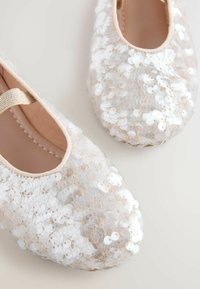 Balletschuhe mit einer semi-transparenten Oberseite aus Pailletten in Weiß und Nude, runder Zehenform und elastischem Riemen für einen sicheren Sitz. Weiche Innenausstattung.
