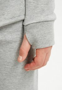 Grauer Baumwoll-Sweatshirt mit einem gerippten Ärmelbündchen, ausgestattet mit einer Daumenöffnung und weicher Textur. Nahaufnahme einer Hand, die auf dem Bündchen ruht.