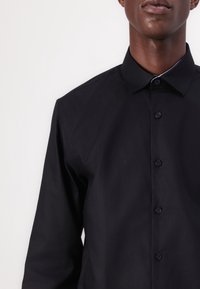 Camicia nera con bottoni, colletto strutturato, tessuto liscio e chiusura con bottoni. Presenta un design minimalista senza motivi o accenti.