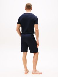 Marineblaues Kurzarm-Polo und passende Shorts. Weicher Stoff, enganliegendes Design und schlichte Textur. Von hinten gesehen, barfuß.