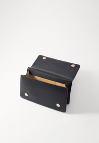 Carteira de couro preta com interior bege, apresentando dois fechos de pressão dourados e uma textura suave. O design aberto revela um amplo espaço de armazenamento.