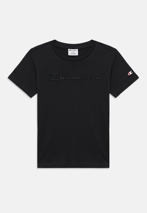 Juoda trumpomis rankovėmis suknelė su siuvineju „Champion“ logotipu priekyje ir mažu „C“ logotipo pleistru kairėje rankovėje.