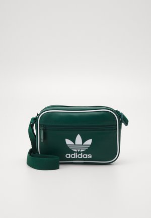 Bolso bandolera verde de Adidas con ribete blanco, bolsillo frontal con cremallera y correa de tela ajustable.