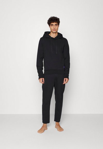 Sweatshirt preto com capuz e mangas compridas, feito de um tecido suave, combinado com calças ajustadas à medida. Ambas as peças têm um design minimalista.