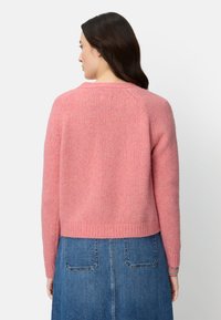 Różowy, miękki sweter dziany o skróconym fasonie, z prążkowanym dołem i raglanowymi rękawami. W zestawie z jeansową spódnicą z tylnymi kieszeniami.