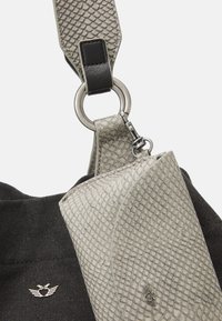 Grijze textuurmateriaal met een slangenhuidpatroon, bevestigd aan een zwarte stoffen tas. Bevat een metalen ring en een logo-accent.
