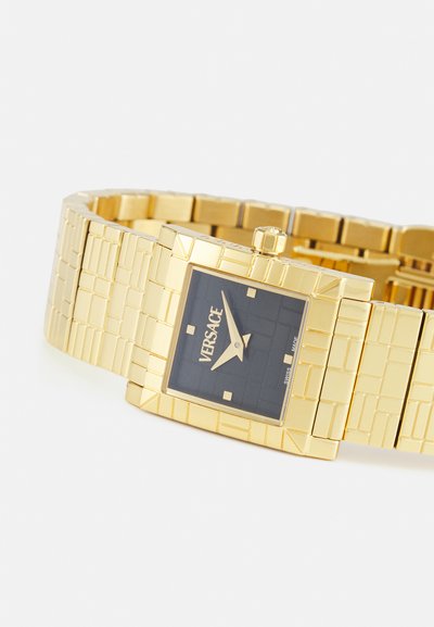 Gold-tone rectangular watch with a textured bracelet, black square dial, and silver hour markers. Features brand name "Versace" on the dial.