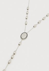 Sudraba ķēdes kaklarota ar ovālas pērļu krelles un centrālu ovālu piekariņu ar teksturētu dizainu, ietvertu ar apaļu krellīšu rāmi.