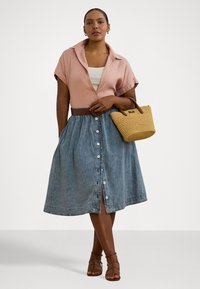 Lys rosa kortermet skjorte, hvit tank topp under, denimskjørt med knapper foran, og vevd stråhåndveske. Brune sandaler med stropper fullfører antrekket.