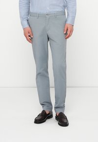 Hellgraue maßgeschneiderte Hosen aus Baumwollmischung mit Knopfverschluss und Seitentaschen, kombiniert mit dunkelbraunen Loafers.