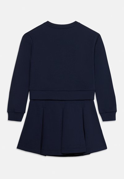 Robe bleu foncé à manches longues avec une ceinture côtelée et une jupe plissée, vue de dos sur un fond blanc uni.