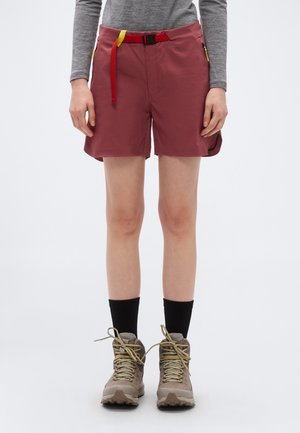 Persoană purtând pantaloni scurți bordo cu curea roșie, cămașă cu mânecă lungă gri, șosete negre și bocanci bej de drumeție, stând pe un fundal alb.