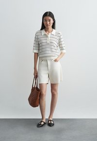 Λευκό και ριγέ πλεκτό πόλο, κρεμ σορτς, καφέ υφαντή τσάντα και μαύρες μπαλαρίνες. Απλός σχεδιασμός με κουμπιά και λεπτομέρειες τσέπης.