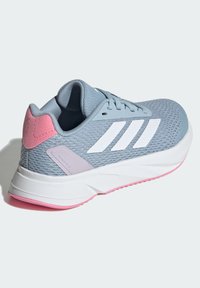 Zapatilla deportiva de malla azul con rayas blancas, talón en acento rosa, puntera redondeada y suela acolchada. Presenta cierre de cordones y material texturizado.