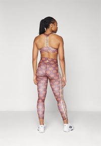 Sport-BH och leggings-set i mauve med orange palmträdsmönster. BH:n har korsade baksnören; leggings har sidostråkar och hög midja.