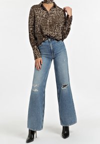 Camicia a maniche lunghe con stampa animalier marrone, abbinata a jeans a vita alta azzurri chiari a gamba larga con dettagli strappati e tacchi a spillo neri.